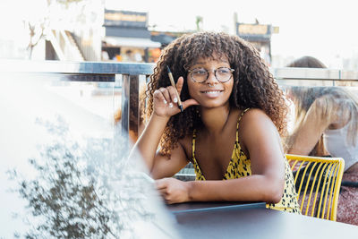 Positive african american female entrepreneur sitting at table on terrace of cafe and thinking about project while looking away