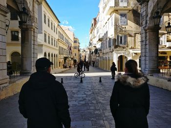 Rear view of people walking on street amidst old buildings in city