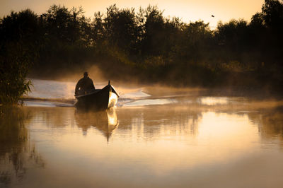 Man riding horse in lake against sky during sunset