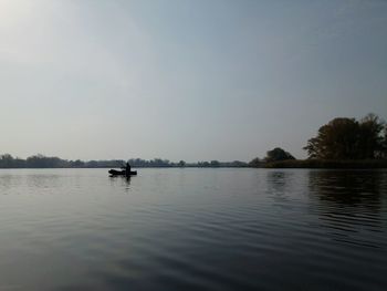 Scenic view of lake against sky with person fishing in background