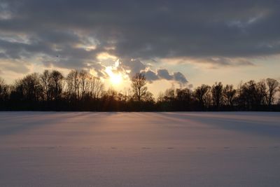 Snow covered landscape against sky during sunset