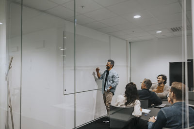 Mature businessman explaining strategy on whiteboard to colleagues in board room