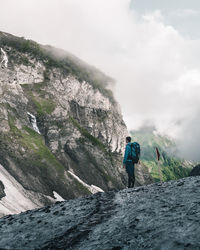 Man walking on rocks by mountain against sky