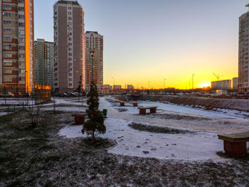 Snow covered buildings against sky during sunset in city