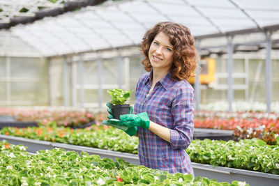 Portrait of woman holding potted plants in greenhouse