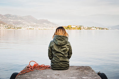 Rear view of woman sitting on pier over lake against sky