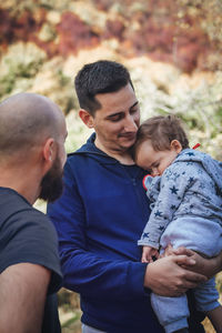 Friend looking at man carrying his sleeping son in forest