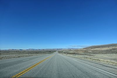 Empty road in desert against clear blue sky