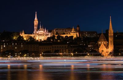 View of illuminated matthias church with river in foreground