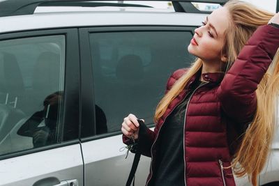 Woman with hand in hair standing by car