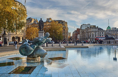 Statue by fountain in city against sky