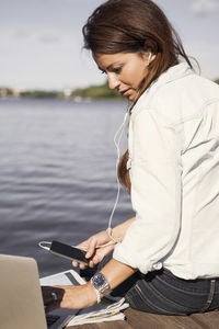 Businesswoman listening music while using laptop on boardwalk at seaside