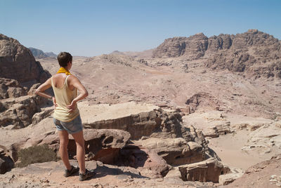 Rear view of woman standing on rock against clear sky