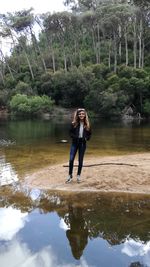 Full length of young woman standing by lake in forest