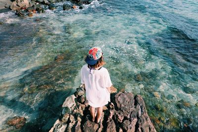 Rear view of woman standing on rock by sea