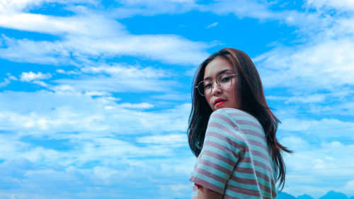 Portrait of young woman standing against blue sky