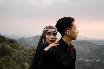 Young couple looking away against mountains and sky