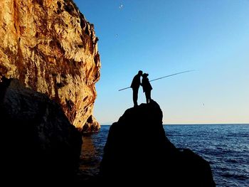 Silhouette man standing on rock by sea against clear sky