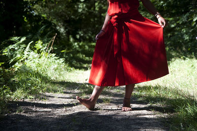 Low section of woman in red dress standing against trees