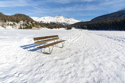 Empty bench on snow covered field against sky