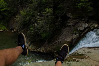 Low section of man standing on rock by river in forest