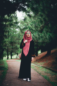 Portrait of young woman standing on footpath amidst trees