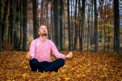 Young man sitting on leaves in forest during autumn