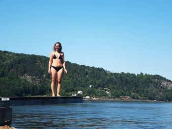 Full length of woman wearing bikini standing by sea on diving platform