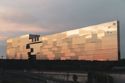 Building by river against sky during sunset