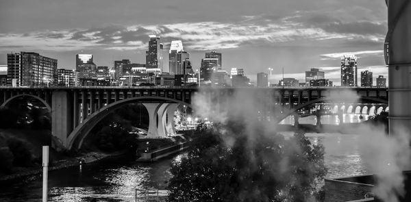 Bridge over river by buildings in city against sky