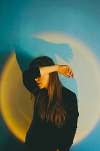 Woman covering face standing in front of illuminated wall