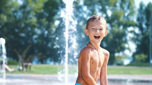 Excited boy of seven years having fun between water jets, in fountain, run around, sprinkle, have