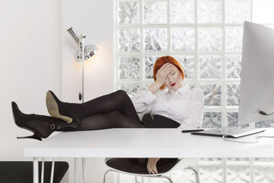 Full length of businesswoman with headache resting legs on desk