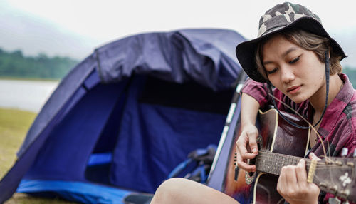 Woman playing guitar while sitting by tent
