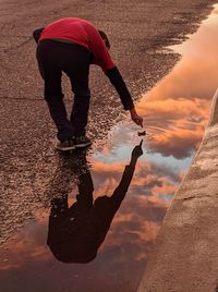 Reflection of men on puddle against sky during sunset