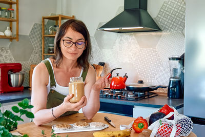 Woman making healthy breakfast or brunch, opening jar with peanut butter for spreading it