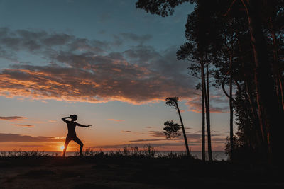 A woman is engaged in karate against the background of the sunset sky