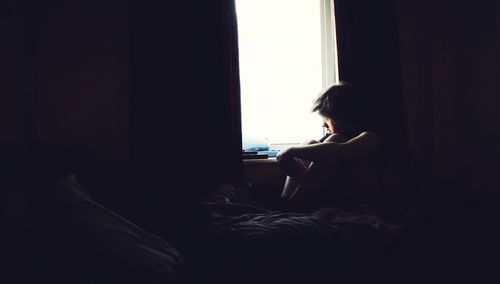 Person sitting by window on bed in room at home