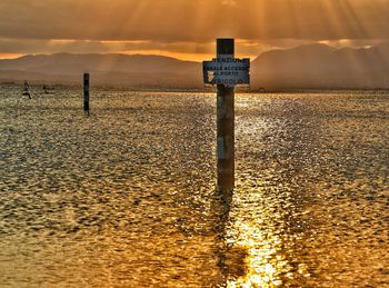 Information sign on wooden post in sea against sky during sunset