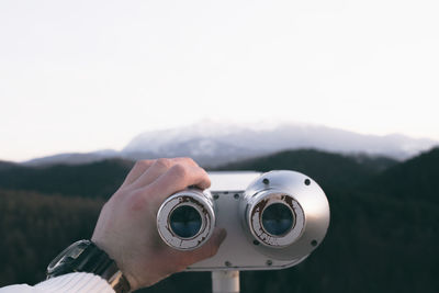 Cropped image of hand holding coin-operated binoculars against mountain