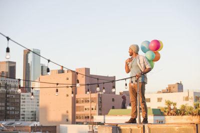 Young man standing on rooftop, holdng balloons