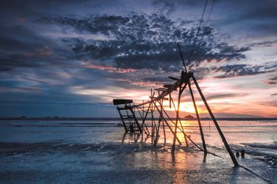 Silhouette cranes on beach against sky during sunset