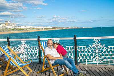 People sitting on railing by sea against sky