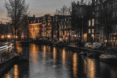 Canal by illuminated buildings in city at night