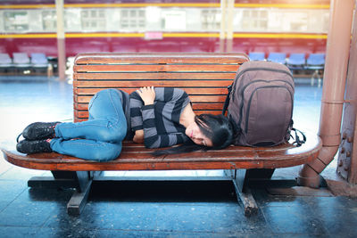 Woman with backpack sleeping on bench at railroad station