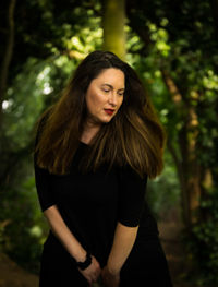 Beautiful young woman standing against trees