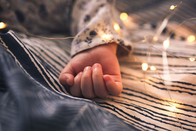 Baby hand close up, the baby is sleeping on the bed, dark blue bedding with an ornament. 