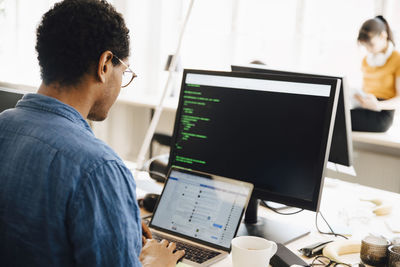 Male computer hacker using laptop on desk while sitting in creative office