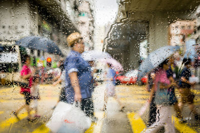 People walking on street seen through wet windshield