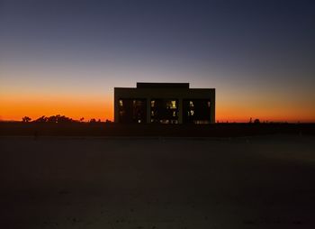 Silhouette building on field against sky at sunset